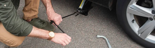 Cropped view of man using lift jack on car, banner — Stock Photo