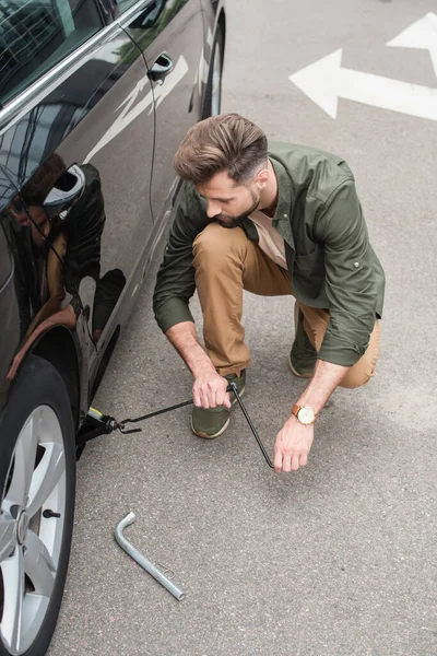 Giovane conducente utilizzando sollevamento jack su auto all'aperto — Foto stock