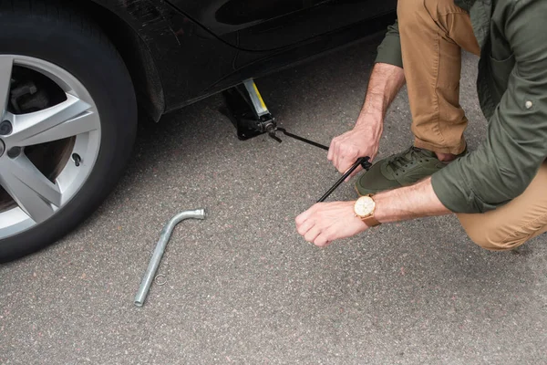 Cropped view of driver using lift jack on car outdoors — Stock Photo