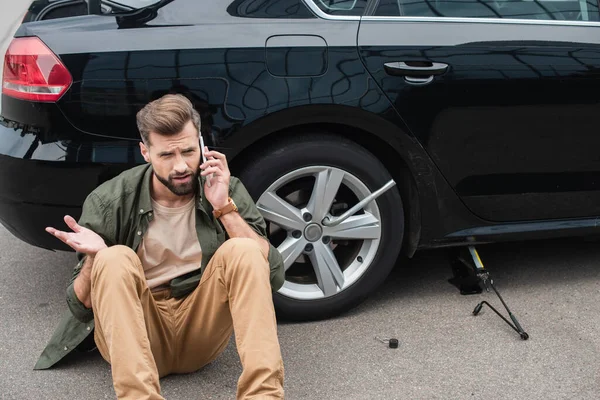 Hombre hablando en el teléfono inteligente cerca del coche con llave de rueda y elevador jack - foto de stock