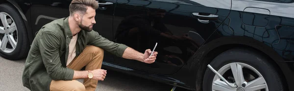 Side view of man taking photo on smartphone of wrench in wheel of car, banner — Stock Photo