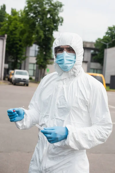 Medical worker in hazmat suit holding pcr test outdoors — Stock Photo