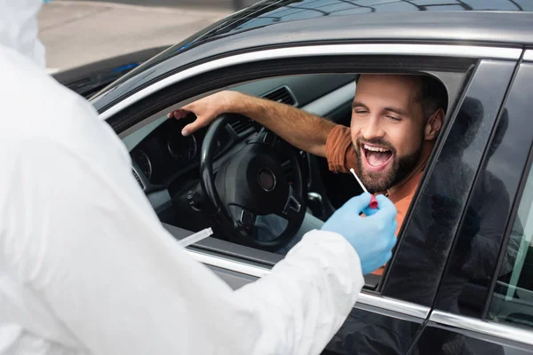 Blurred medical worker holding pcr test near driver with open mouth in auto — Stock Photo