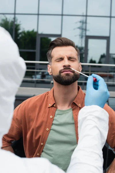 Uomo con gli occhi chiusi in piedi vicino operatore medico con test PCR all'aperto — Foto stock