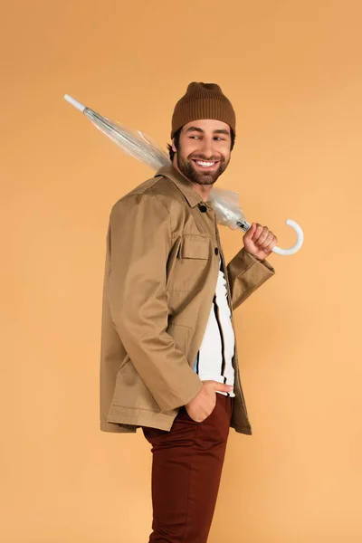Fröhlicher Mann mit gefaltetem Schirm, der die Hand in der Tasche hält, isoliert auf beige — Stockfoto