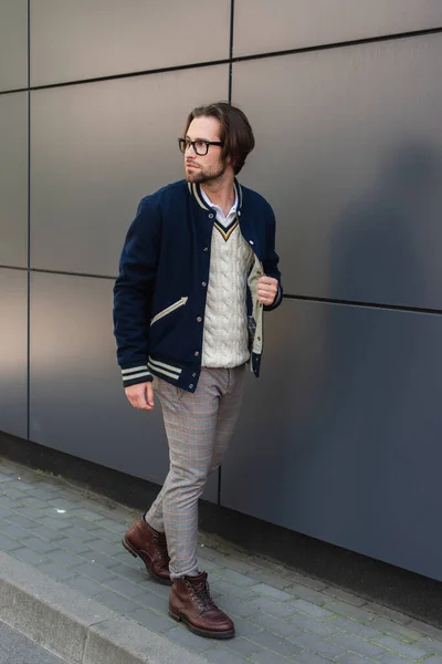 Молодий чоловік в модному одязі дивиться далеко під час прогулянки по сірій стіні — стокове фото