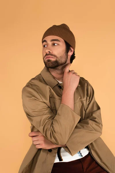 Young man in trendy jacket and beanie looking away isolated on beige - foto de stock