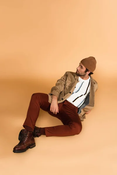 Young man in stylish autumn outfit sitting on beige background - foto de stock