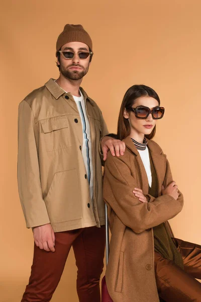 Fashionable woman sitting with crossed arms near trendy man isolated on beige — Fotografia de Stock