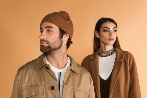 Trendy man in beanie looking aside near blurred stylish woman isolated on beige — Foto stock