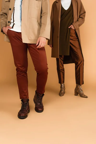 Abgeschnittene Ansicht eines Paares in modischer Herbstkleidung, das mit Händen in Taschen auf beigem Hintergrund posiert — Stock Photo