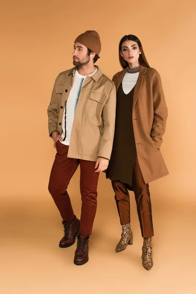 Full length view of couple in trendy autumn clothes standing on beige background — Fotografia de Stock