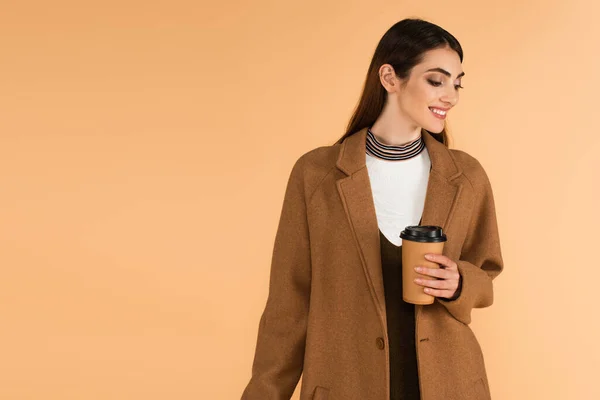 Happy woman in stylish coat holding takeaway drink isolated on beige — Foto stock