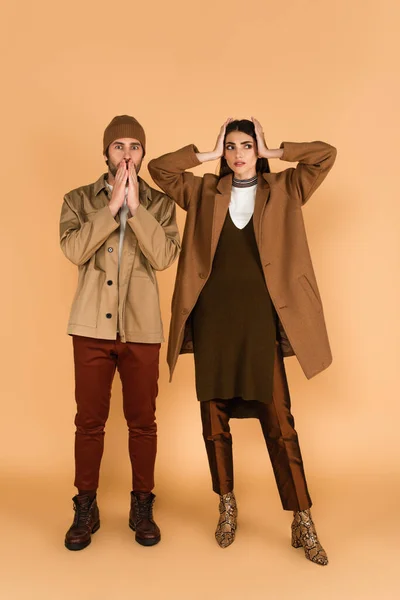 Worried man in jacket and beanie near stylish woman touching head on beige background — Stock Photo