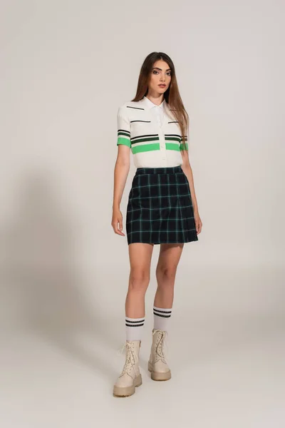 Full length view of young woman in plaid skirt and high boots on grey background - foto de stock