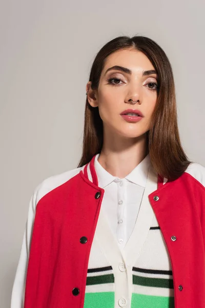 Young brunette woman in red and white jacket looking at camera isolated on grey — Photo de stock