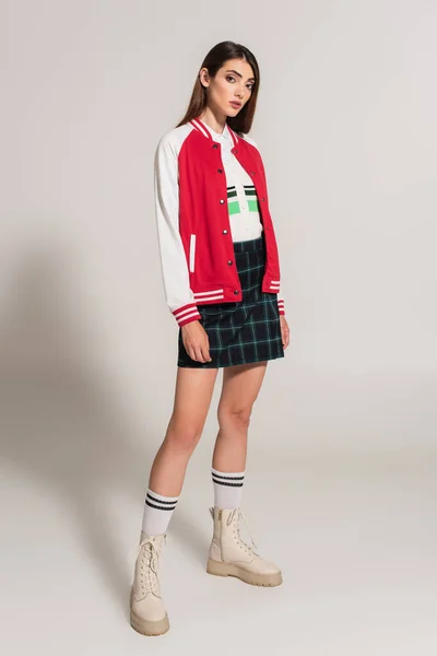 Young woman in stylish jacket, plaid skirt and high boots posing on grey background — Photo de stock