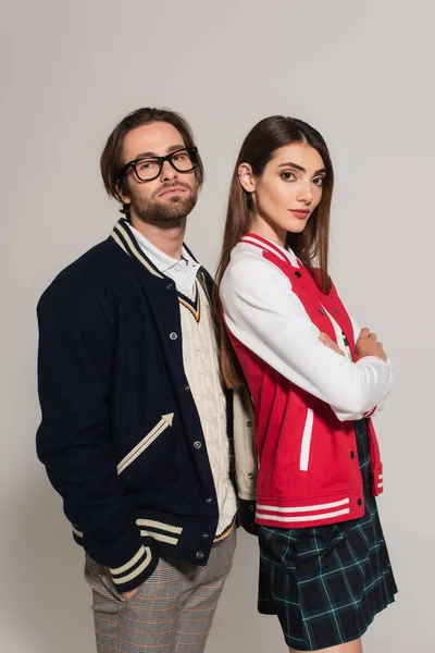 Young woman in stylish jackets looking at camera while posing near man isolated on grey - foto de stock