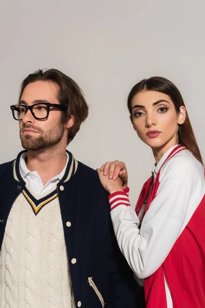 Brunette woman in red and white jacket looking at camera near man in eyeglasses isolated on grey — Fotografia de Stock