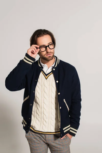 Man in blue jacket adjusting eyeglasses while standing with hand in pocket on grey — Photo de stock