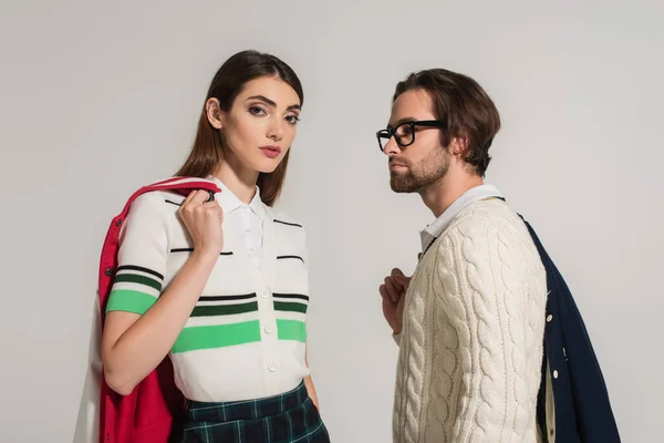 Brunette woman in striped polo t-shirt looking at camera near man in white jumper isolated on grey — Photo de stock