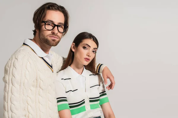 Man in white knitted pullover embracing shoulder of stylish brunette woman isolated on grey — Stock Photo