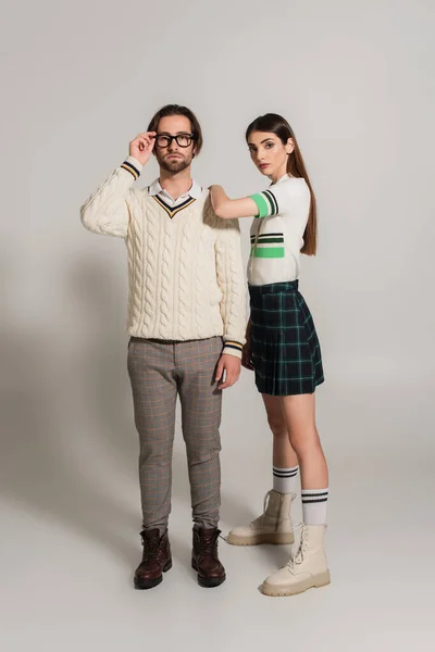 Мужчина в белом пуловере настраивает очки рядом с женщиной, опирающейся на его плечо на сером фоне — стоковое фото