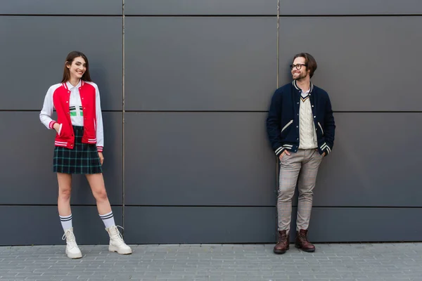 Happy couple in fashionable clothes posing near grey wall outdoors — Fotografia de Stock