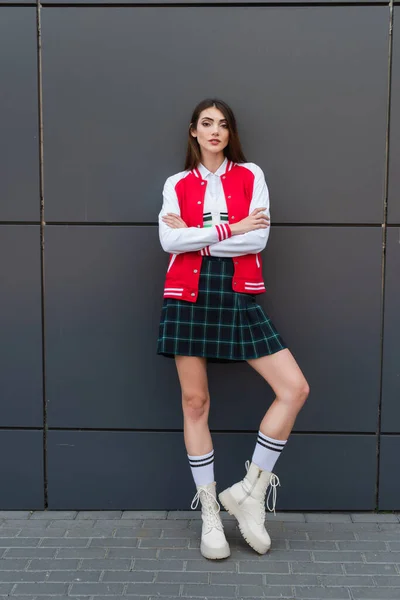 Full length view of woman in stylish jacket, plaid shirt and leather boots near grey wall — Stock Photo