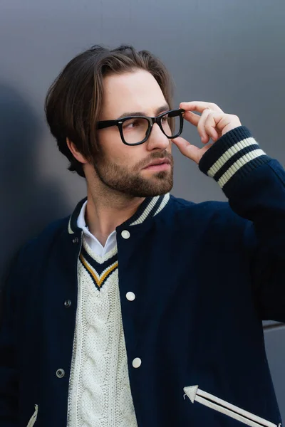 Fashionable man in pullover and jacket adjusting eyeglasses while looking away — Fotografia de Stock