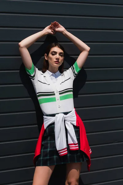 Young woman in striped polo t-shirt posing near grey wall with raised hands — Fotografia de Stock