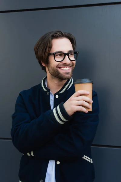 Cheerful man with coffee to go looking away near grey wall outdoors — Fotografia de Stock