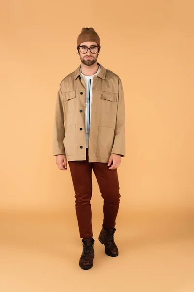 Full length view of man in brown pants and jacket looking at camera on beige background - foto de stock