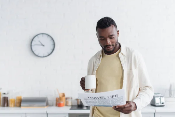 Молодой африканский американец держит чашку кофе и читает газету о жизни во время путешествий — стоковое фото