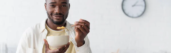 Cheerful african american man holding bowl with corn flakes, banner — Stock Photo