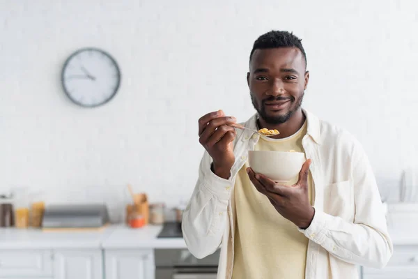 Cheerful african american man holding bowl with corn flakes — Stock Photo