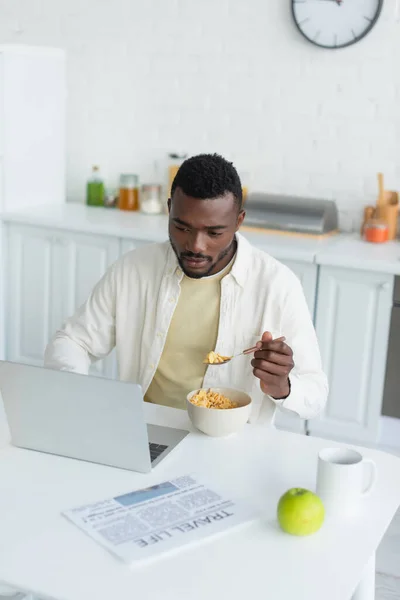 Joven afroamericano hombre usando portátil y desayunando - foto de stock