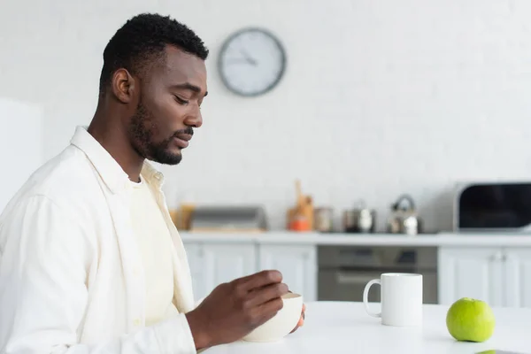 Hombre afroamericano desayunando cerca de manzana y taza de café - foto de stock