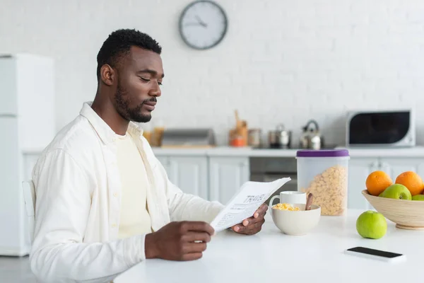 Hombre afroamericano leyendo periódico durante el desayuno - foto de stock