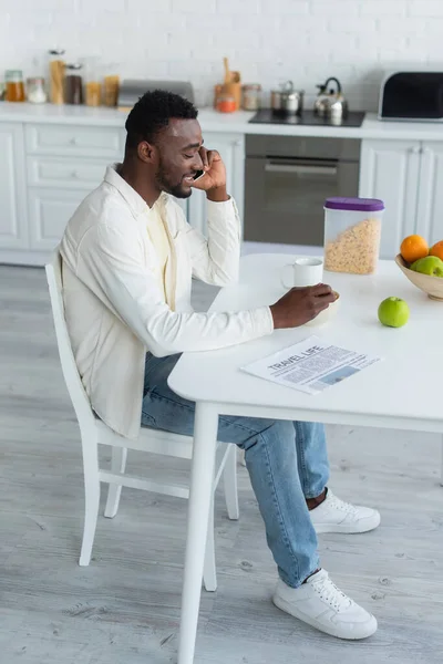 Alegre afroamericano hombre hablando en smartphone mientras desayuna - foto de stock