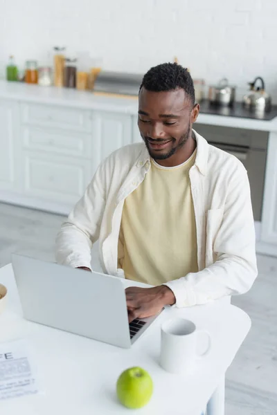 Freelancer afroamericano feliz escribiendo en el ordenador portátil - foto de stock