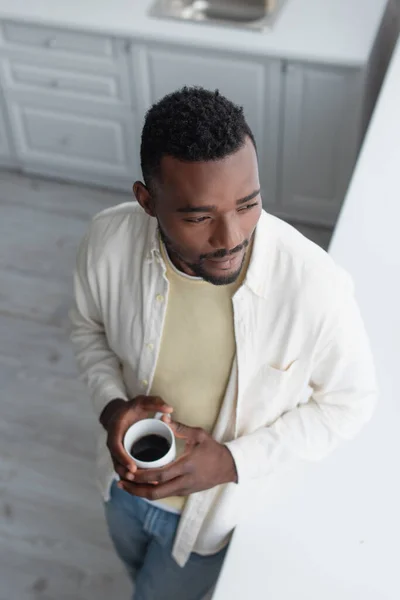 Blick aus der Vogelperspektive auf einen afrikanisch-amerikanischen Mann mit einer Tasse Kaffee in der Küche — Stockfoto