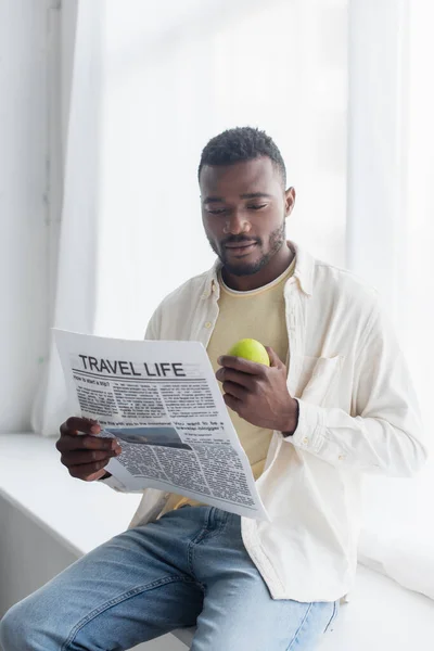Afroamericano hombre sosteniendo manzana y leyendo viaje vida periódico - foto de stock