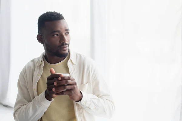 Pensive african american man holding cup of coffee in morning — Stock Photo