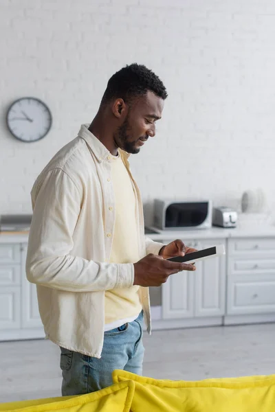 Vista laterale di sorridente uomo africano americano utilizzando tablet digitale con schermo bianco — Foto stock