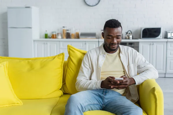 Alegre joven afroamericano hombre mensajes de texto en smartphone - foto de stock