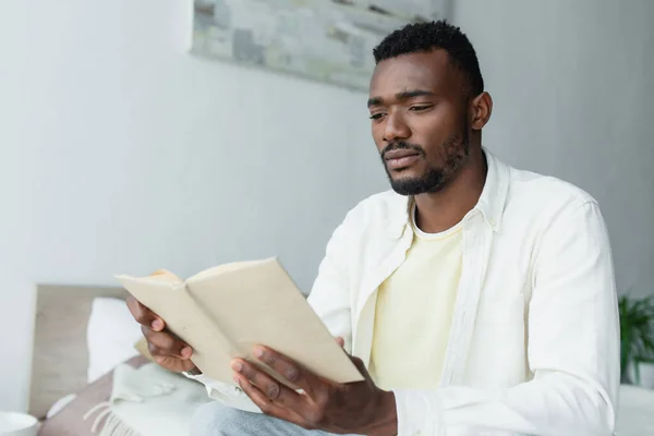 Joven afroamericano hombre leyendo libro en casa - foto de stock