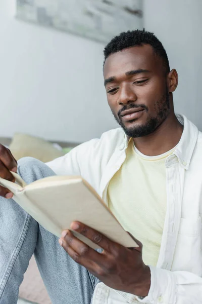 Joven afroamericano hombre lectura borrosa libro en casa - foto de stock