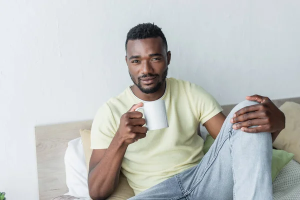 African american man holding cup of coffee in bedroom — Stock Photo