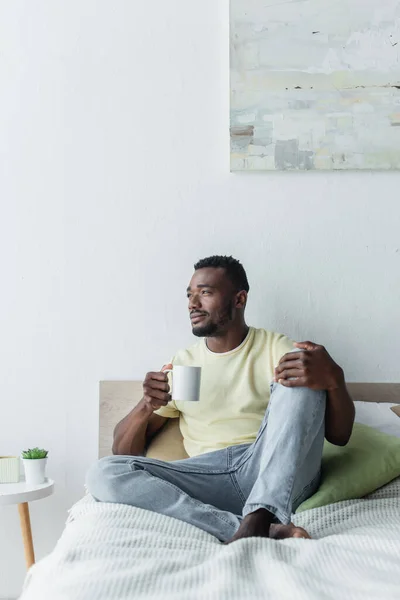 Afrikanisch-amerikanischer Mann hält Tasse Kaffee in der Hand und schaut im Schlafzimmer weg — Stockfoto